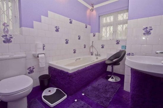 The bathroom features a bath surrounded by shagpile and purple tiles even
