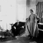 England. 1955. Lady Norah Docker models an elegant gown as her husband Sir Bernard Docker looks on.